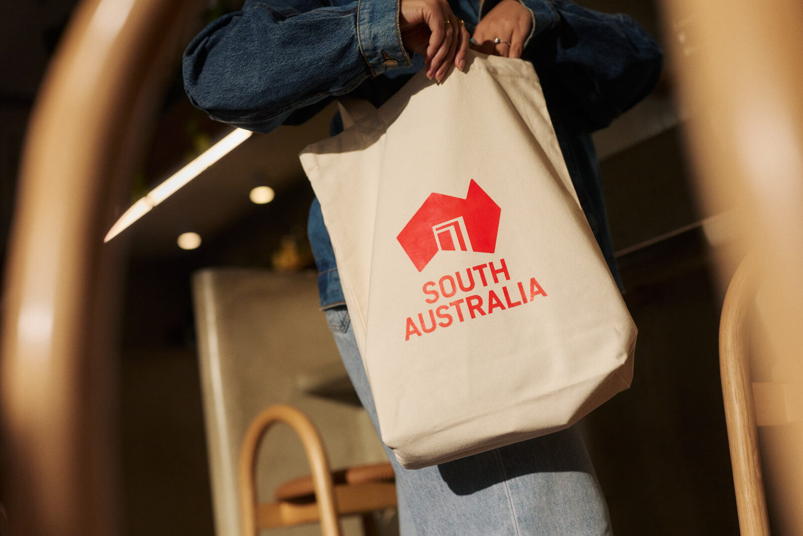 A person dressed in denim, holding a branded South Australia tote bag