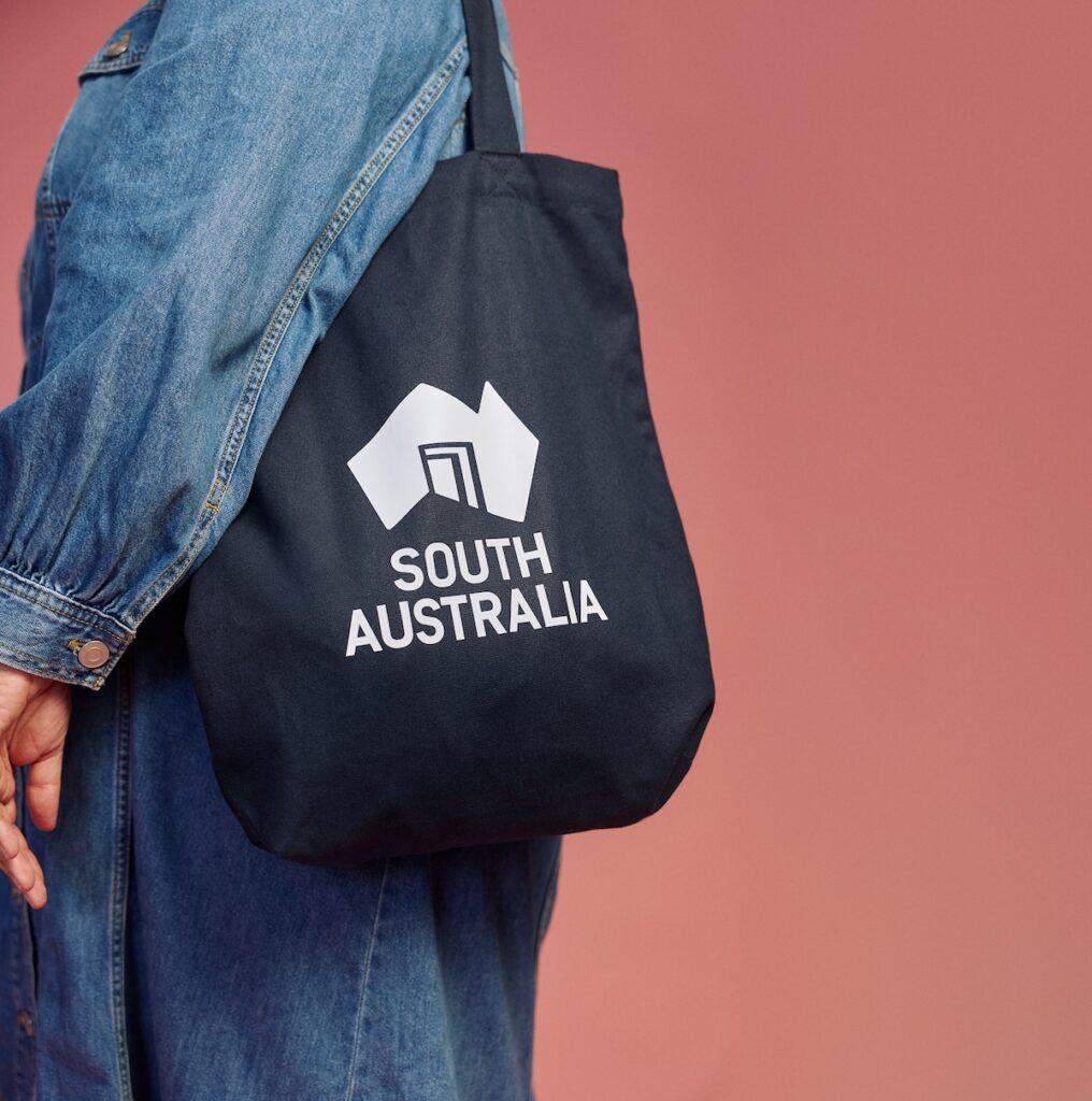 A person wearing denim, with a navy branded South Australia tote bag on their shoulder