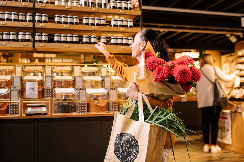 A person shopping at Adelaide Central market holding flowers and a bag full of product