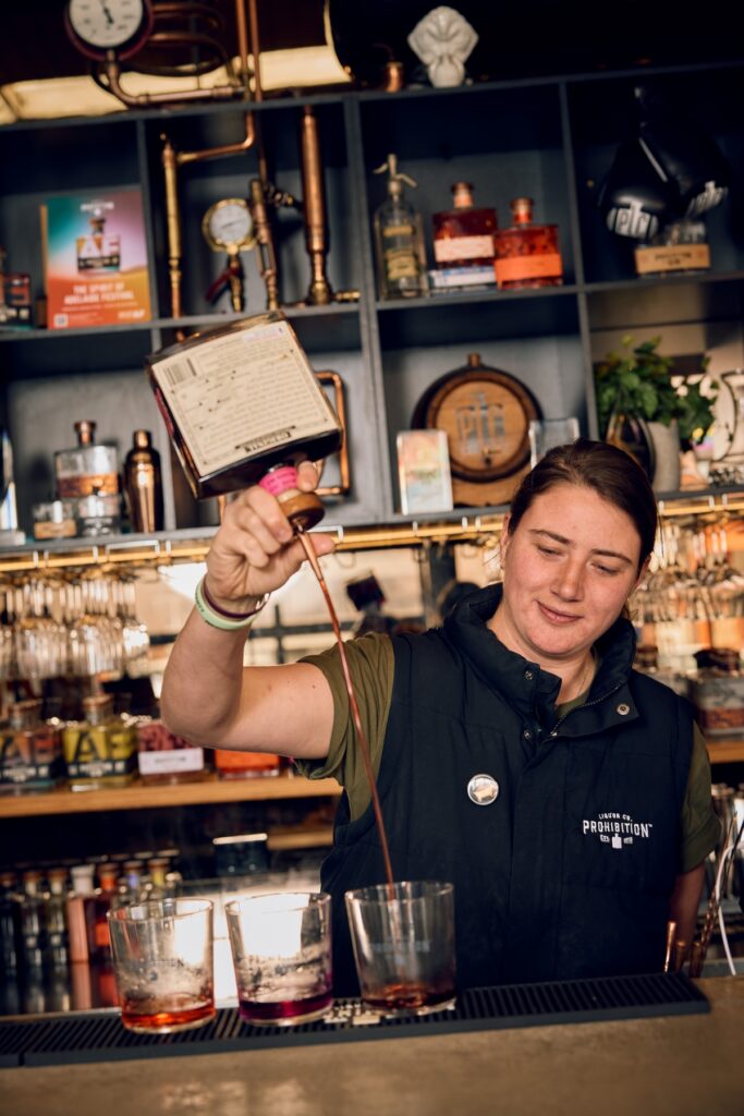 A bar tender pouring spirits into glasses on a bar