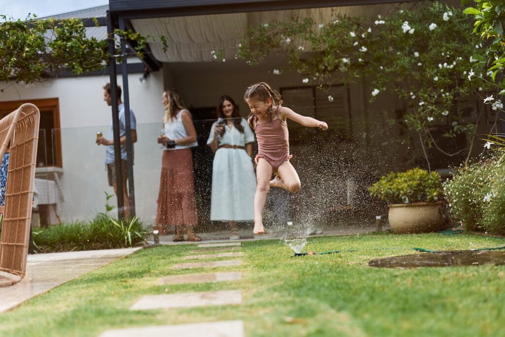 child running through backyard sprinkler