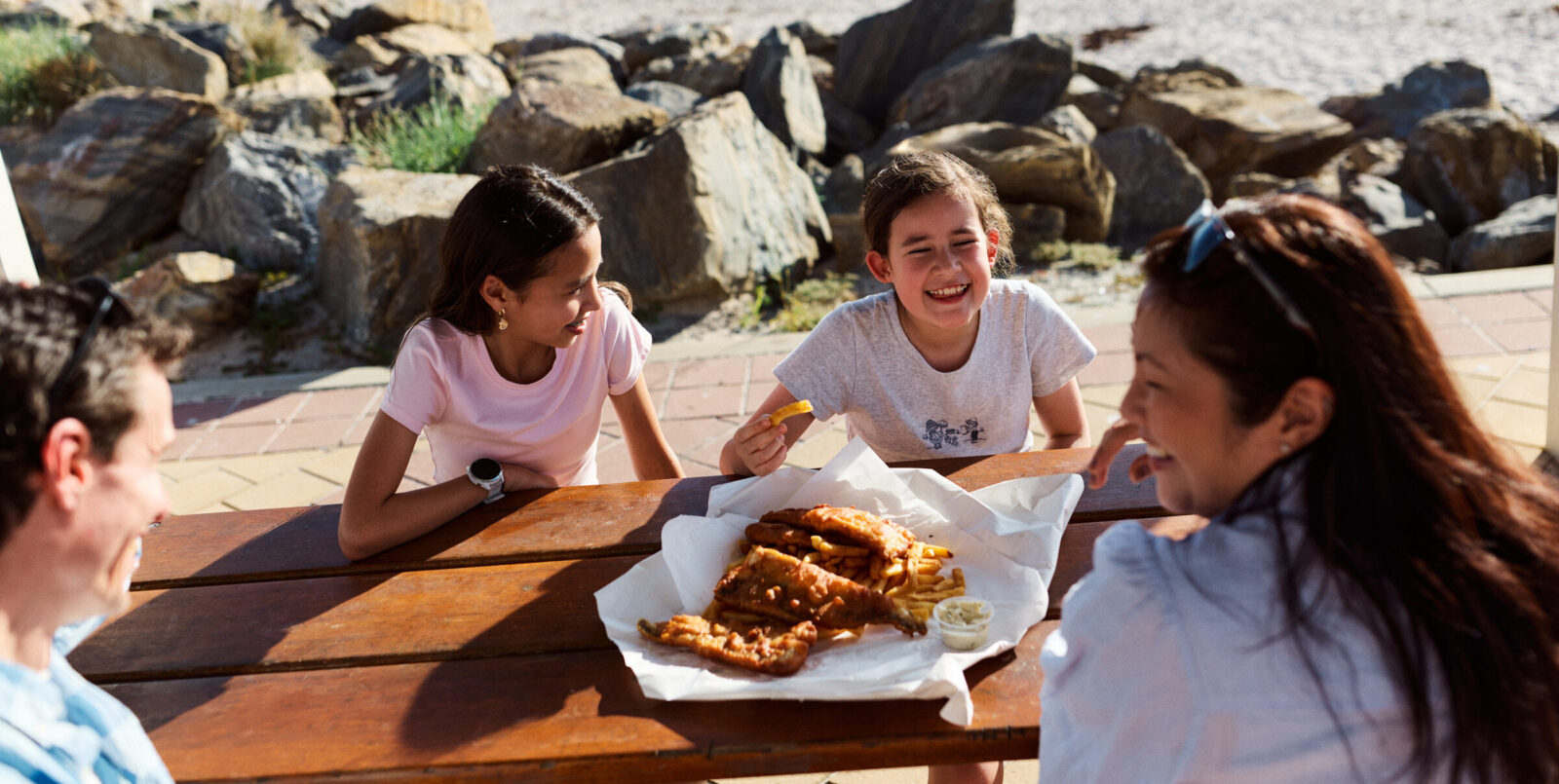 A family eating fish and chips on a table at the beach