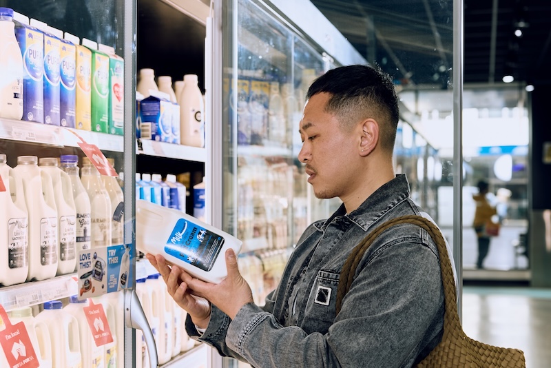 A man standing at the Milk section in a supermarket, with the fridge door open looking at a carton of milk