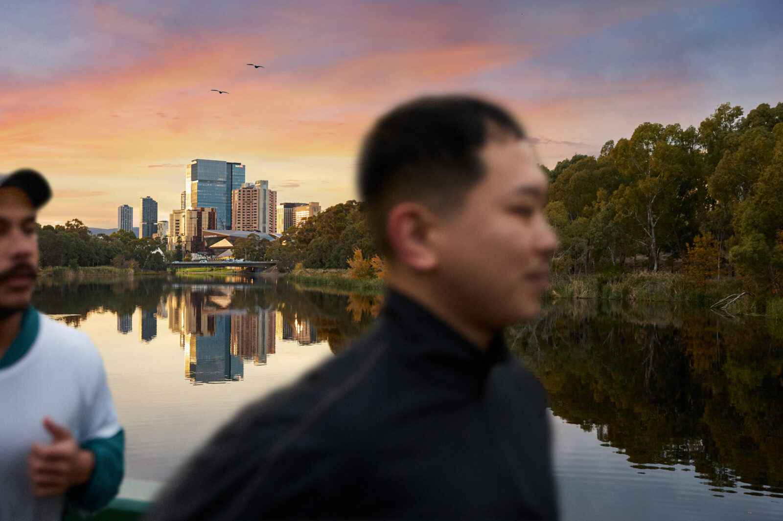 a person running along the Torrens River, with the South Australian city scape in the background