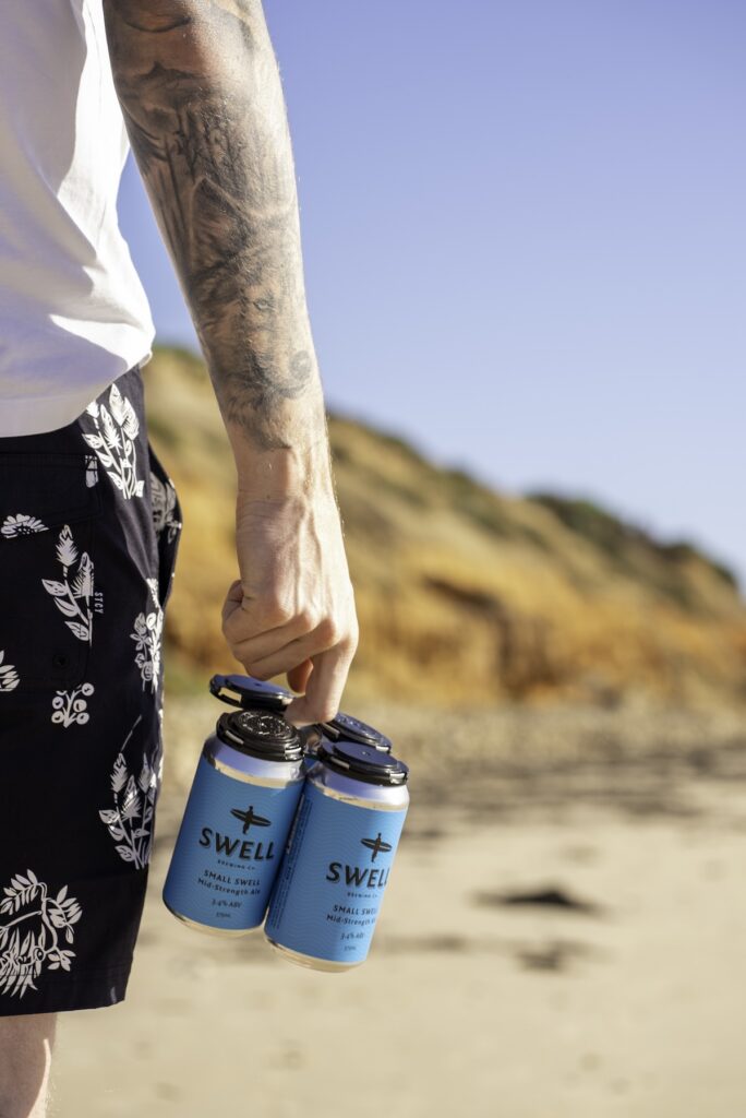 A person walking on the beach holding a pack of Swell drinks