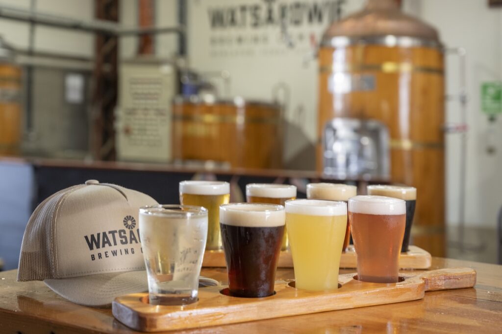A tasting paddle of beer on a table with a branded hat at Watsacowie Brewery