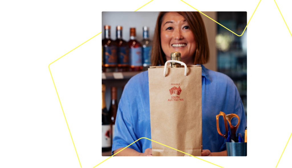 Person smiling toward camera holding a paper bag with the Proudly South Australian logo.