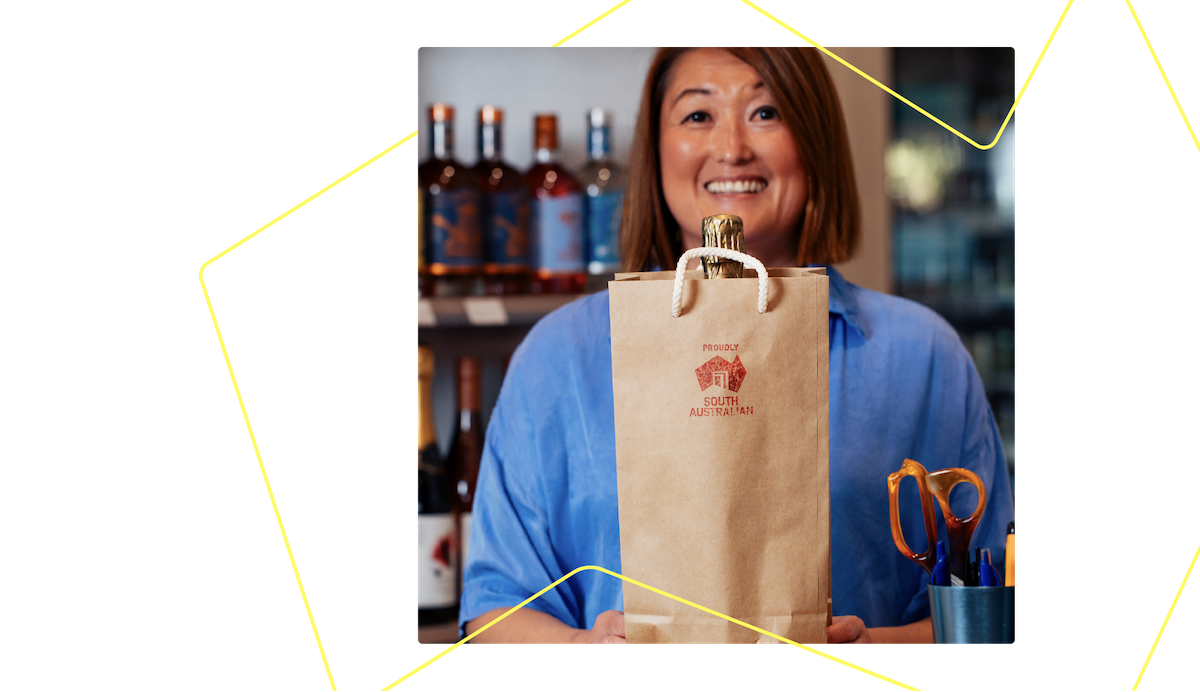 Person smiling toward camera holding a paper bag with the Proudly South Australian logo.