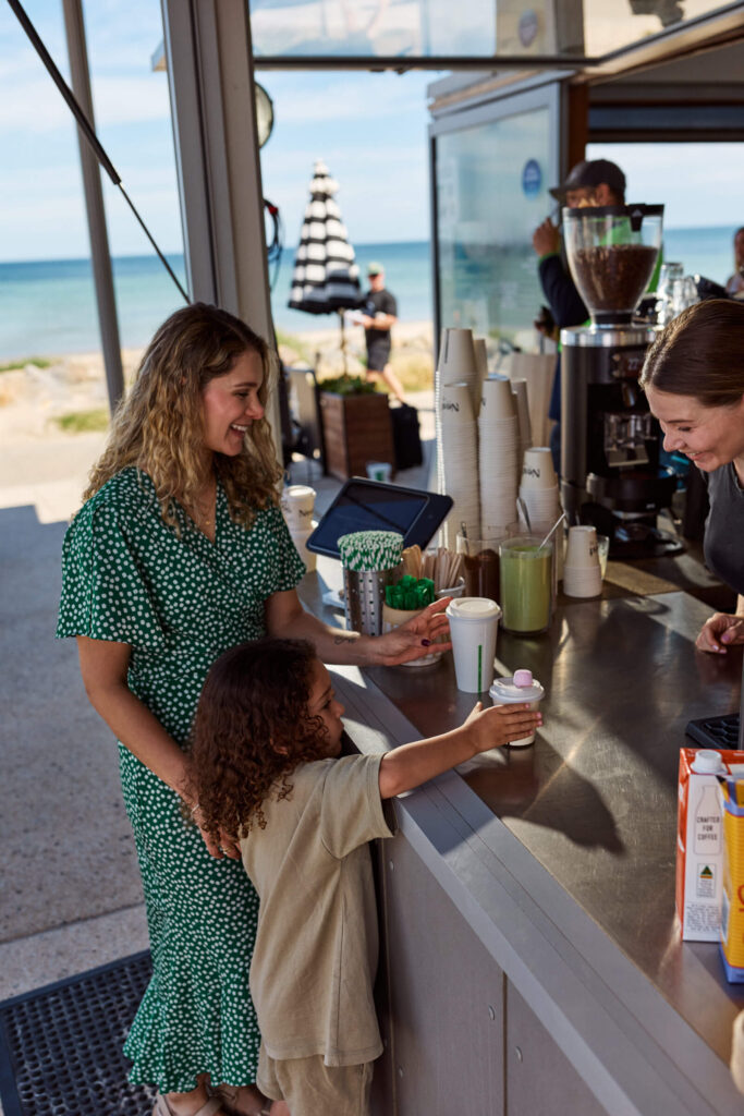 Mother and child at a beachside cafe counter picking up hot drinks