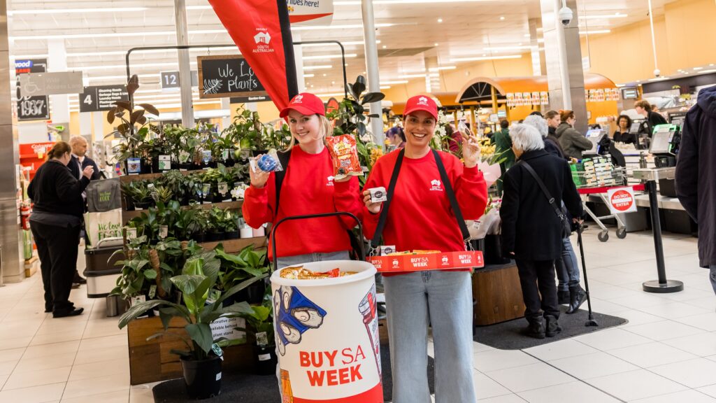 They Buy SA stall in Rundle mall with two people holding up cans of softdrink and packets of popcorn whilst smiling towards each other